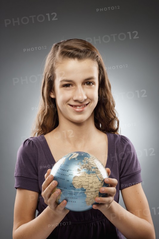 Portrait of girl (12-13) holding globe and looking at camera, studio shot. Photo : FBP
