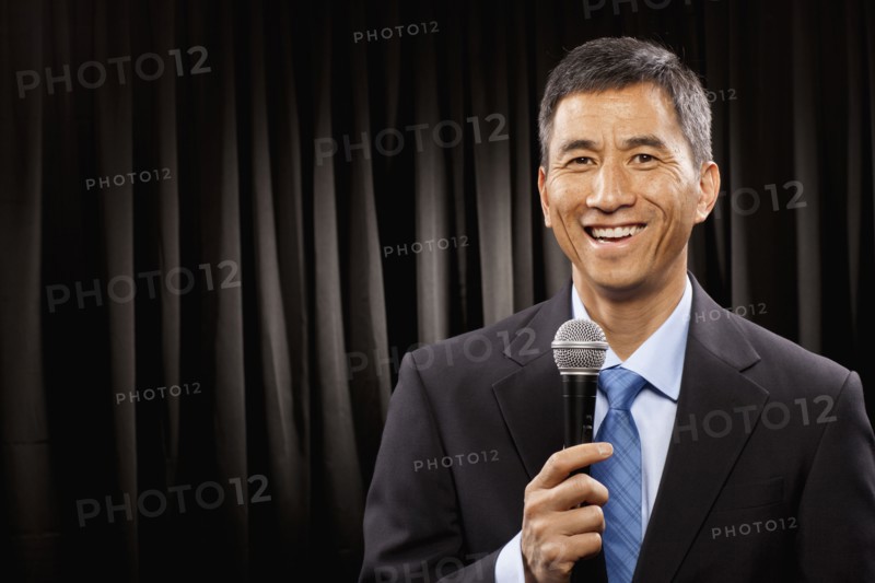 USA, Utah, Provo, Portrait of businessman with microphone standing in front of black curtain. Photo : FBP