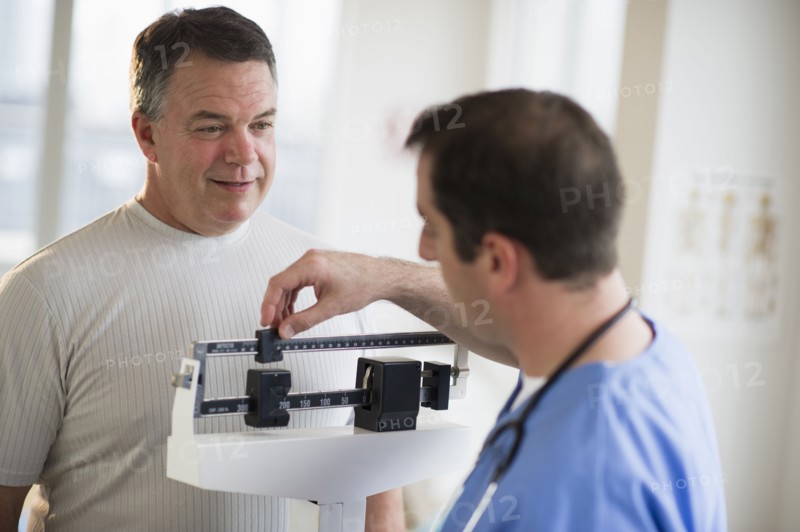USA, New Jersey, Jersey City, Doctor assisting male patient on weighing scales in hospital.