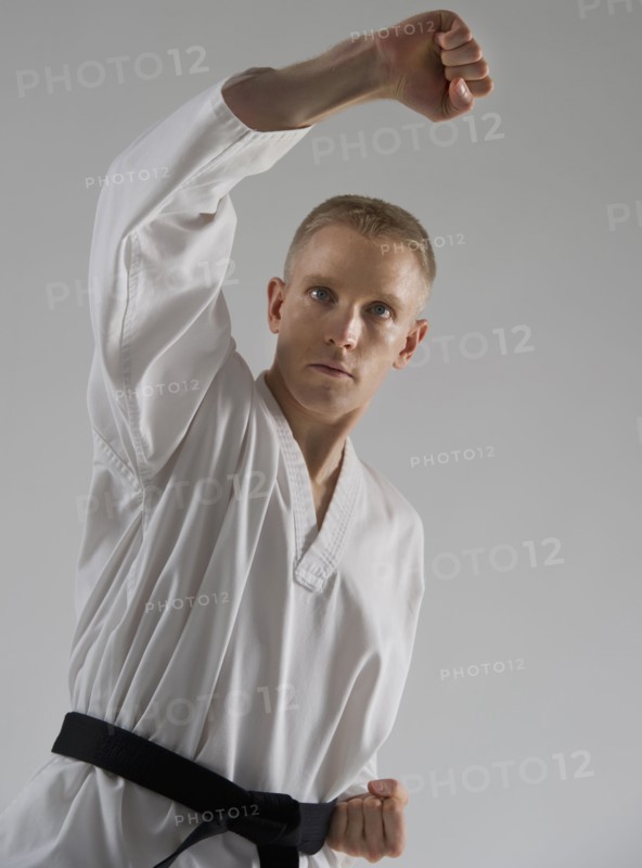 Young man performing karate stance on white background.