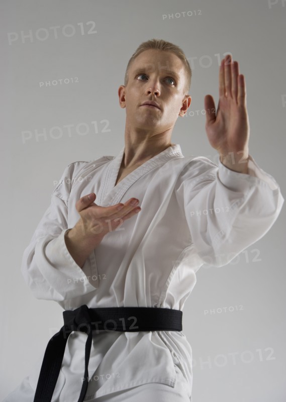Young man performing karate stance on white background.