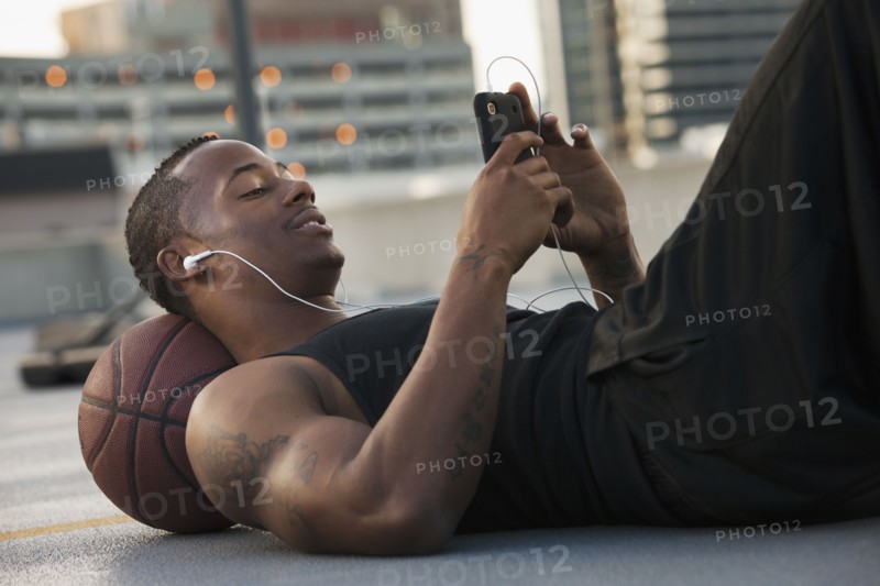 USA, Utah, Salt Lake City, Young man lying on basketball and listening to mp3 player. Photo : Mike Kemp