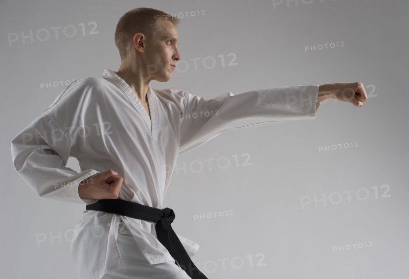 Young man performing karate stance on white background.