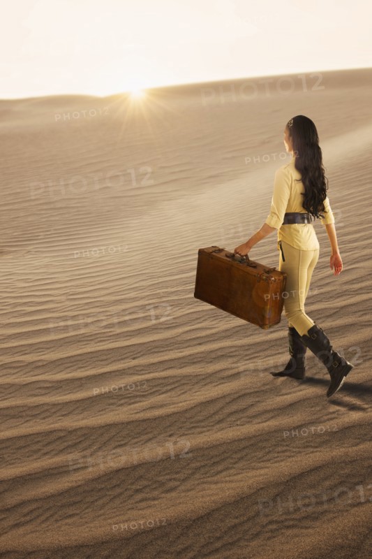USA, California, Death Valley, Woman with suitcase walking in desert.