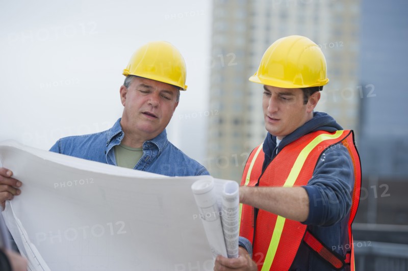 USA, New Jersey, Jersey City, Construction workers studying blueprints on construction site.