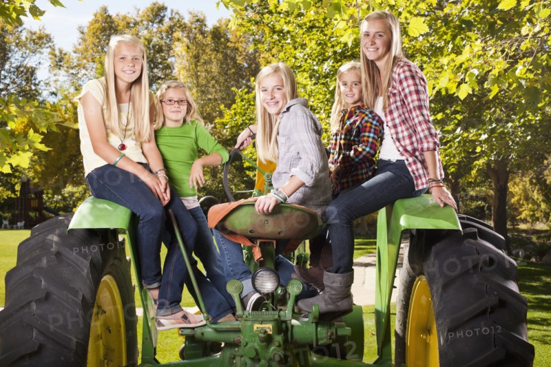 USA, Utah, family portrait of sisters (6-7, 8-9, 12-13, 14-15, 16-17) sitting on tractor. Photo : Tim Pannell