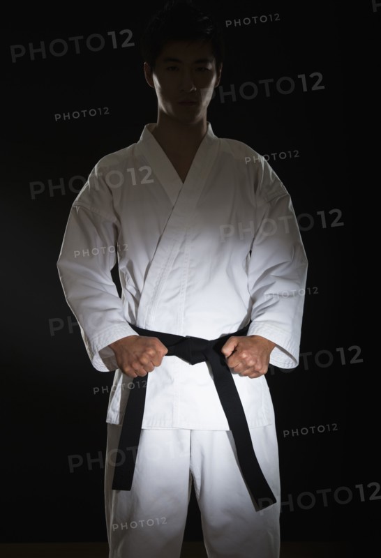 Portrait of young man performing karate stance on black background.