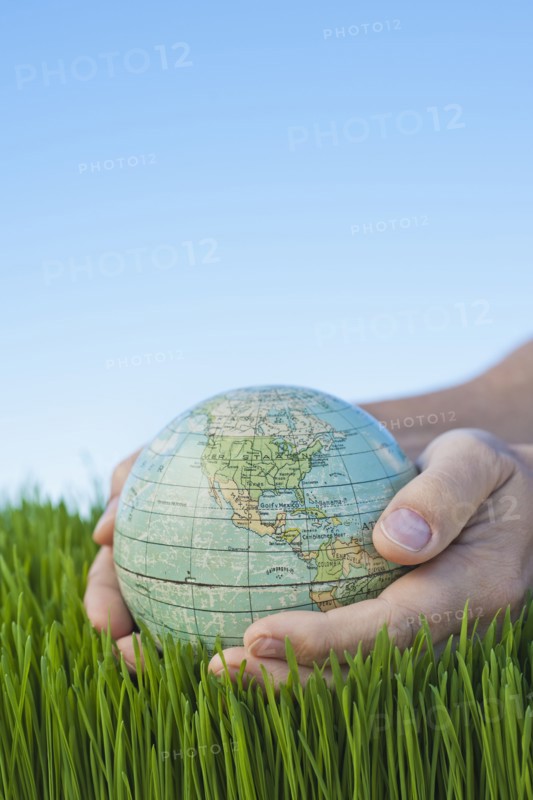 Male hands holding globe over grass.