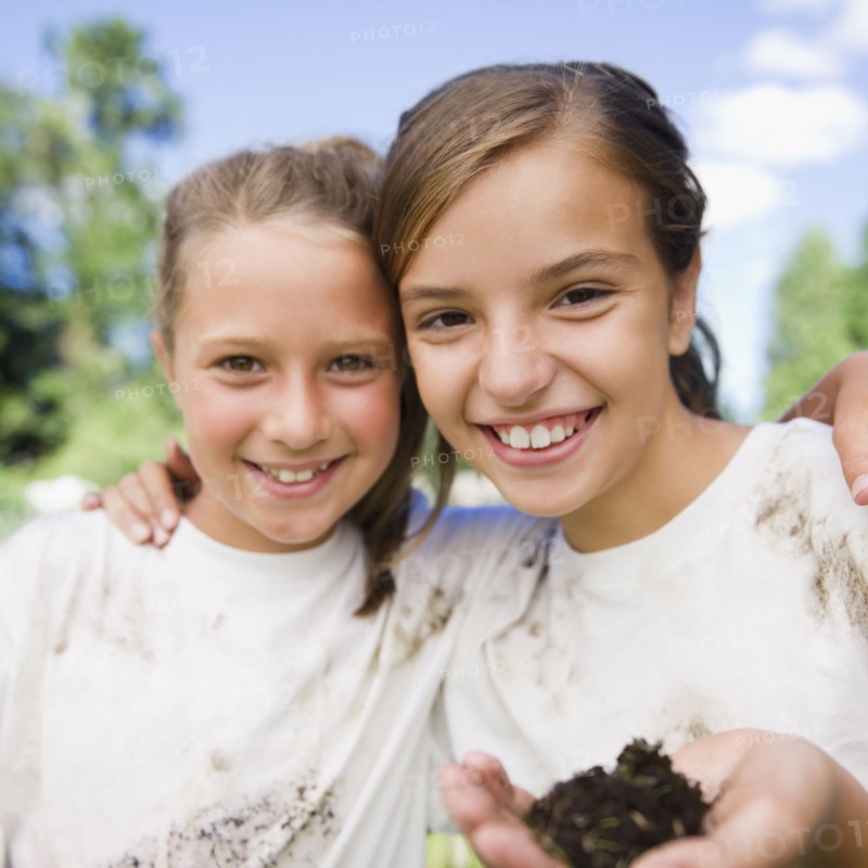 USA, New York, Two girls (10-11, 10-11) holding soil wearing dirty t-shirts. Photo : Jamie Grill Photography