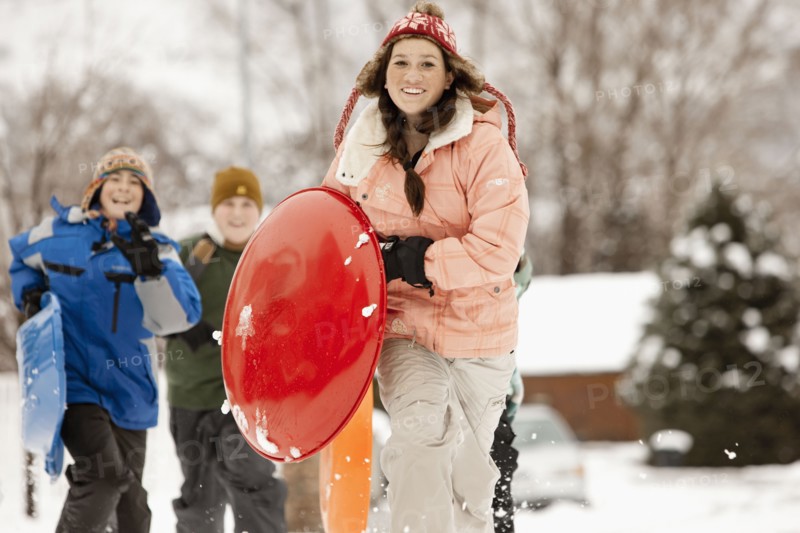 USA, Utah, Provo, Teenage (16-17) girl running with sledge, boys and girls (10-11, 12-13) in background. Photo : FBP