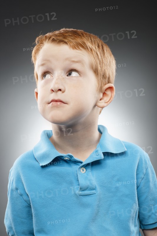 Portrait of smiling redhead boy (4-5) wearing blue polo shirt and looking up, studio shot. Photo : FBP