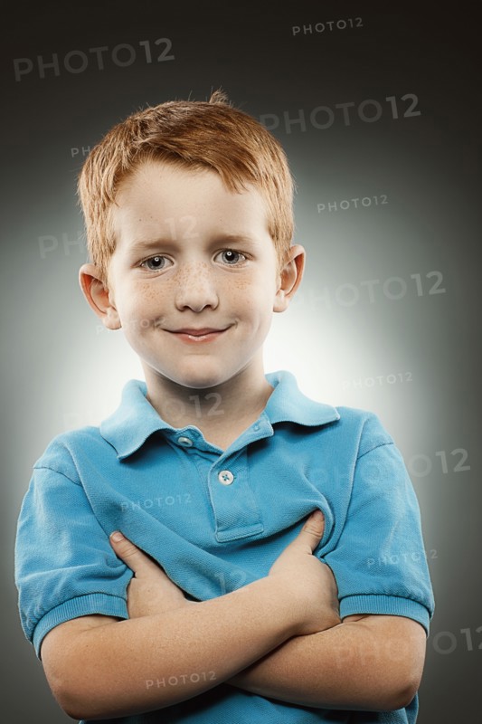 Portrait of smiling redhead boy (4-5) wearing blue polo shirt with arms crossed, studio shot. Photo : FBP