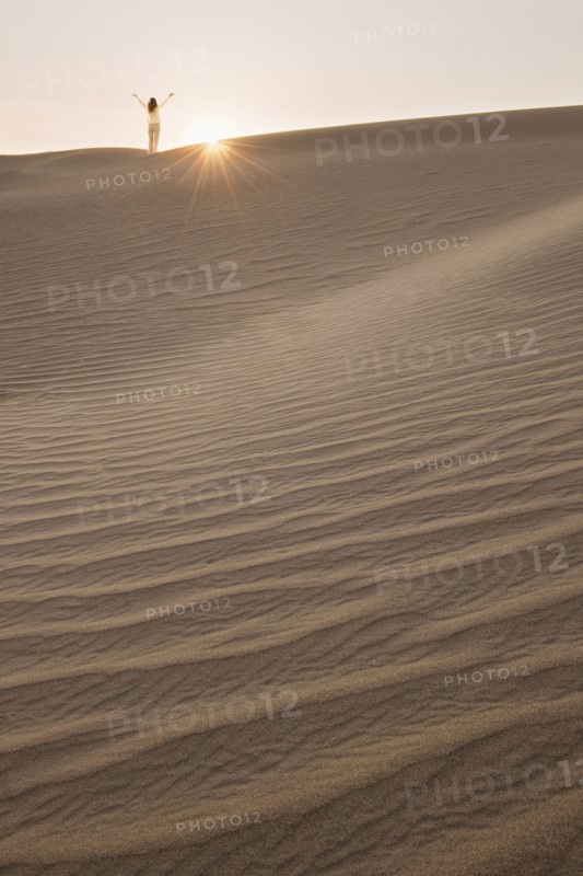Woman with arms up, standing in desert.