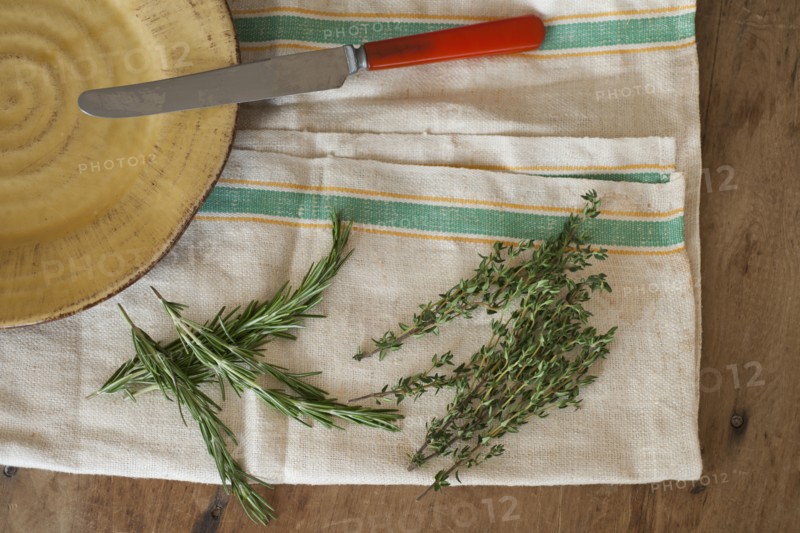 Rosemary and thyme with kitchen knife lying on kitchen cloth, directly above.