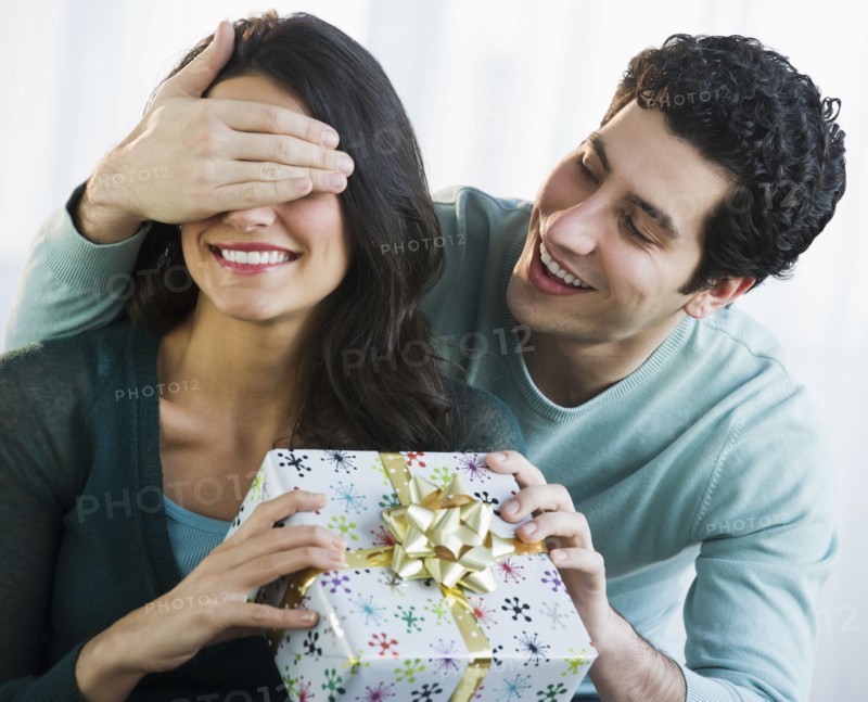 Young man giving his girlfriend present while covering her eyes. Photo : Daniel Grill
