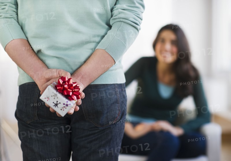 Young man with present behind his back, girlfriend in background. Photo : Daniel Grill