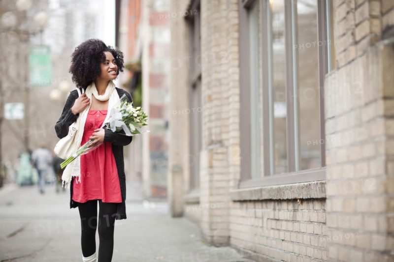 USA, Washington State, Seattle, Young woman walking in street carrying bunch of tulips. Photo : Take A Pix Media