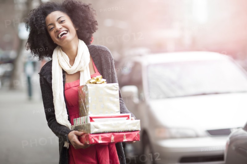 USA, Washington State, Seattle, Young cheerful woman carrying stack of boxed gifts. Photo : Take A Pix Media