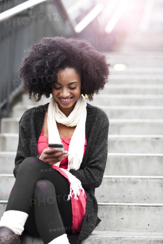 USA, Washington State, Seattle, young woman sitting on steps and text messaging. Photo : Take A Pix Media