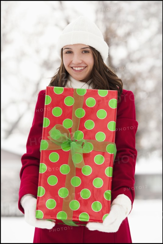 USA, Utah, Lehi, Portrait of young woman holding Christmas gift outdoors. Photo : Mike Kemp