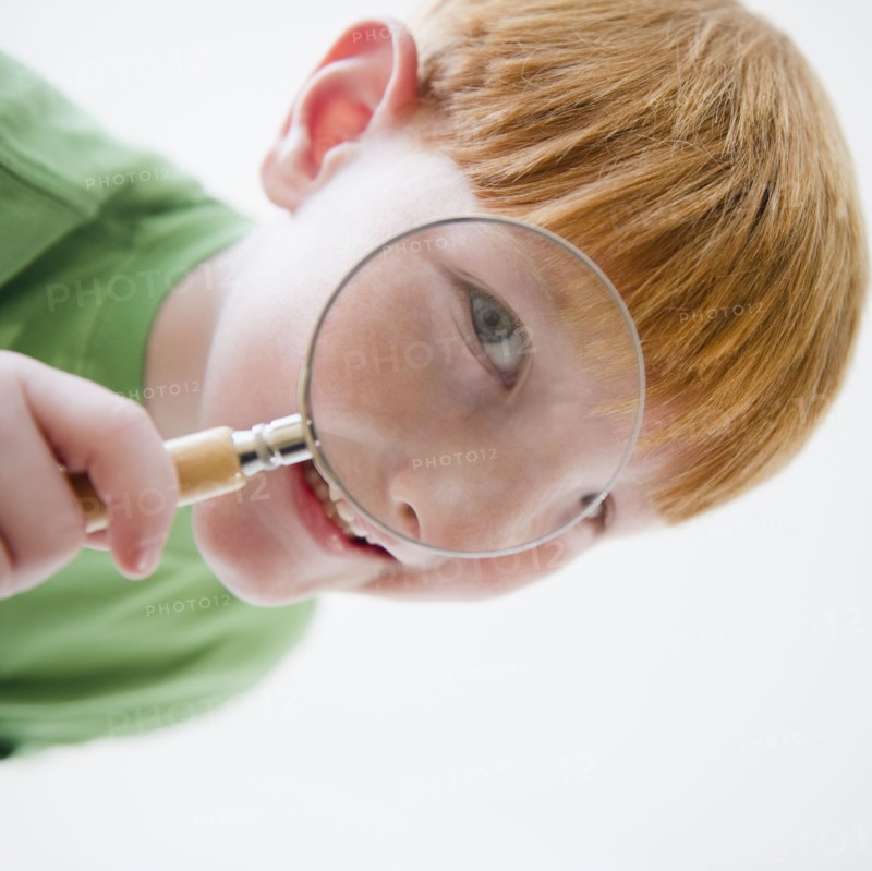 Portrait of boy (8-9) looking through magnifying glass. Photo : Jamie Grill Photography