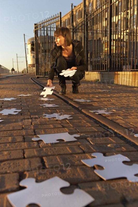 USA, New York City, Brooklyn, woman picking up jigsaw pieces from sidewalk. Photo : Shawn O'Connor