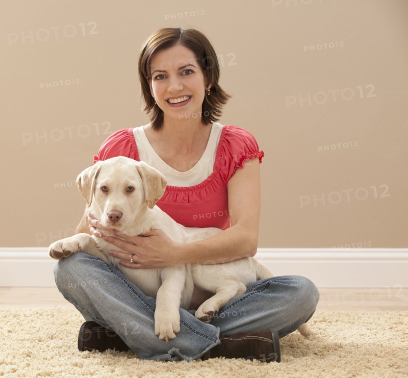 Portrait of woman embracing Labrador on carpet. Photo : Mike Kemp