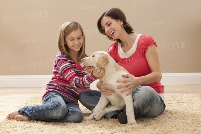 Mother and daughter (10-11) playing with Labrador on carpet. Photo : Mike Kemp