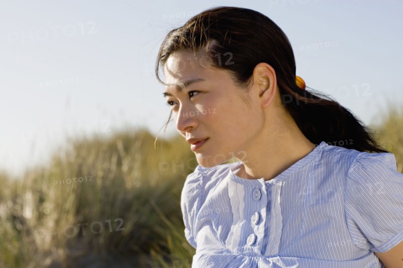 USA, California, Point Reyes, Young woman sitting in grass on sand dune. Photo : Noah Clayton
