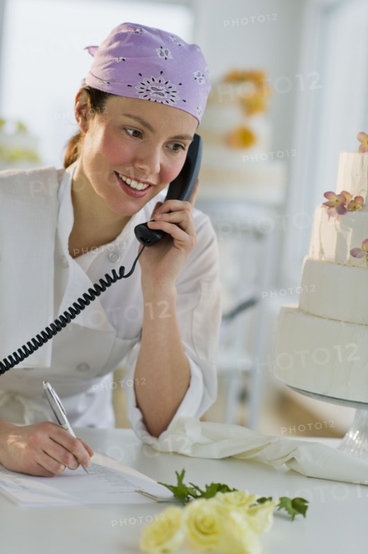 Happy young woman taking order near wedding cake.