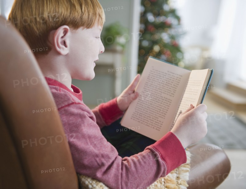 Boy (8-9) reading book on Christmas Eve. Photo : Jamie Grill Photography