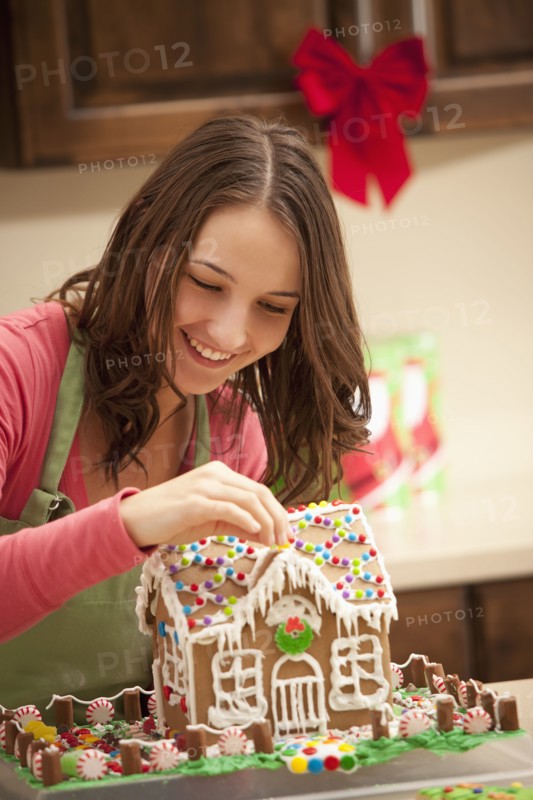 Young woman decorating gingerbread house in kitchen. Photo : Mike Kemp