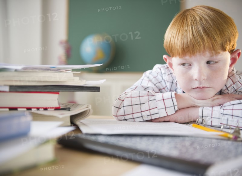 Boy (8-9) sitting at crowded desk in classroom. Photo : Jamie Grill Photography