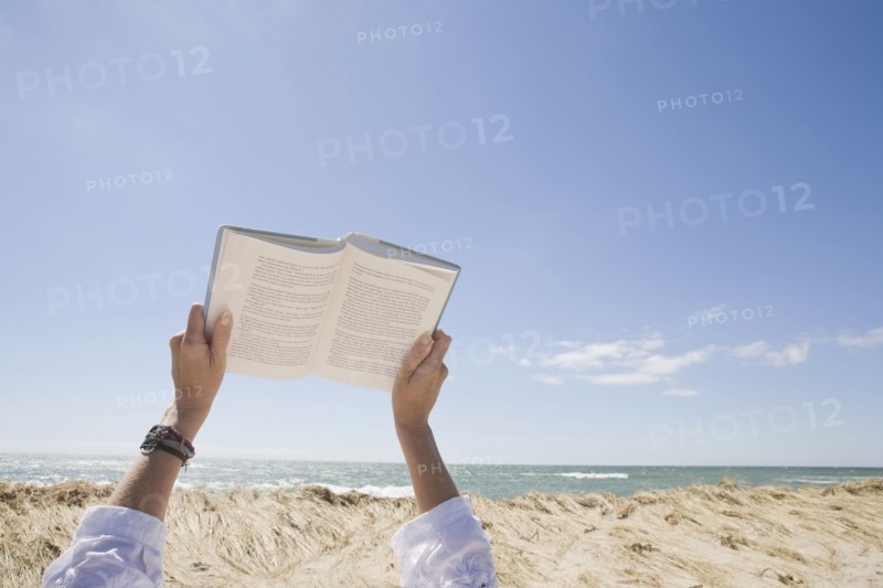 USA, Massachusetts, woman's hands on beach holding book. Photo : Chris Hackett