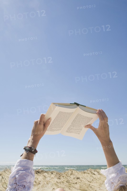 USA, Massachusetts, woman's hands on beach holding book. Photo : Chris Hackett