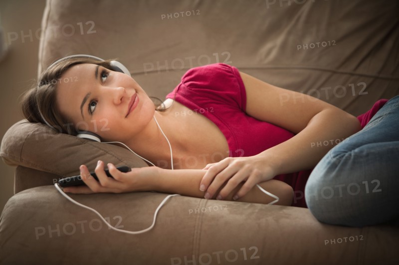 Young woman lying down on sofa and listening music . Photo : Mike Kemp