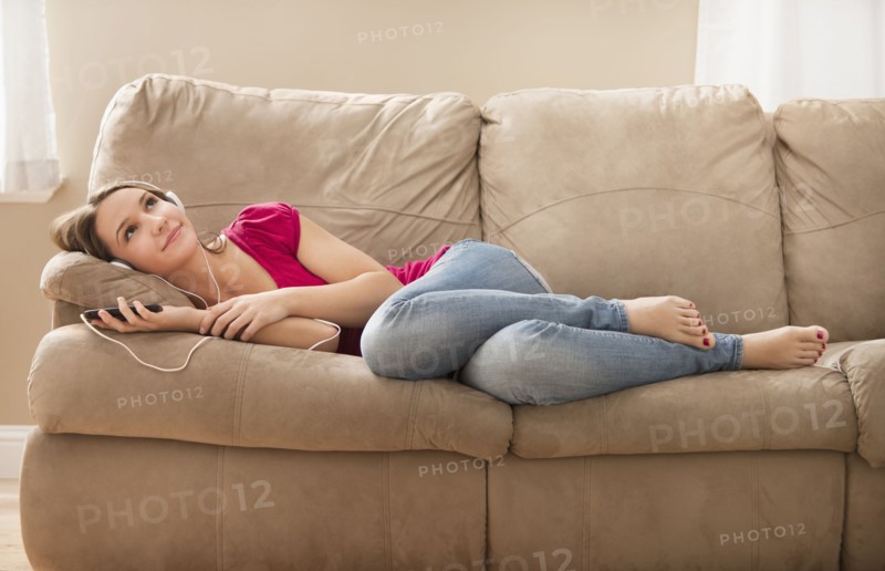 Young woman lying down on sofa and listening music . Photo : Mike Kemp