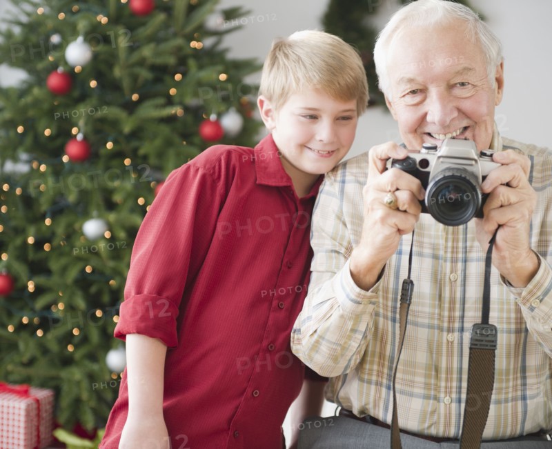 Grandfather and grandson (8-9 years) taking picture, christmas tree in background. Photo : Jamie Grill Photography