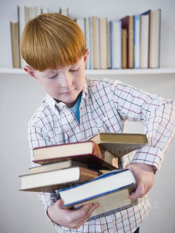 Boy (8-9) carrying stacked books. Photo : Jamie Grill Photography