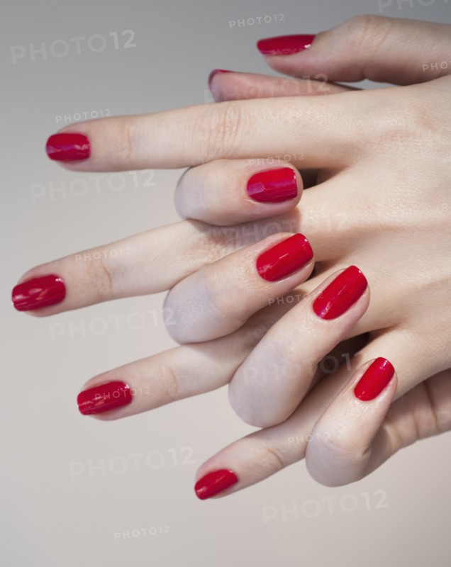 Close up of woman's clasped hands with red nail polish.