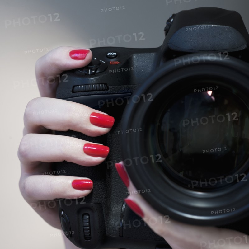 Close up of woman's hand with red nail polish holding camera.