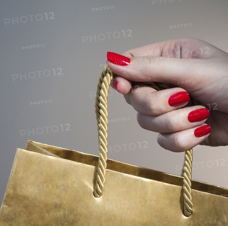 Close up of woman's hand with red nail polish holding string handle of paper bag.