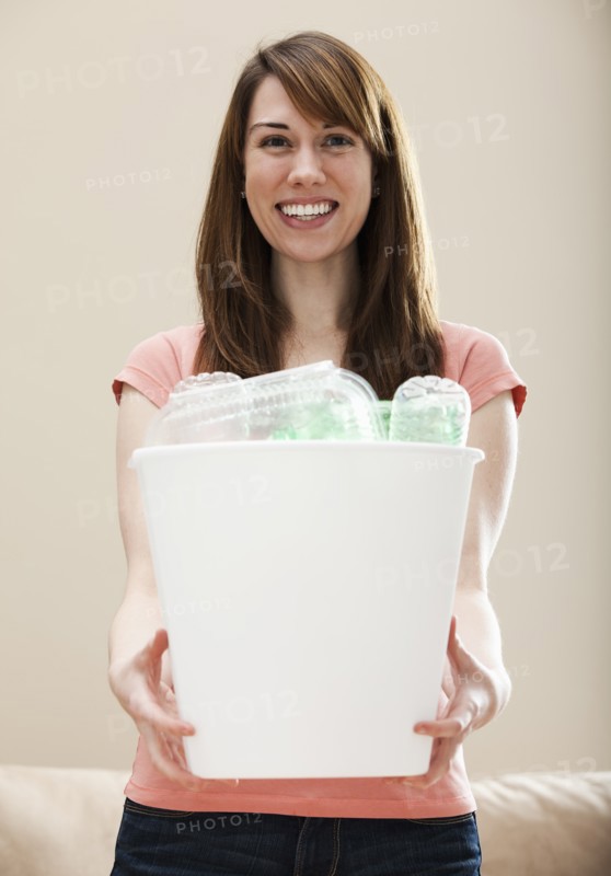 Studio portrait of smiling woman holding recycling bin in plastic bottle. Photo: Mike Kemp