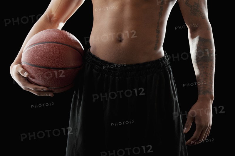 Studio shot of shirtless man holding basketball, mid section. Photo : Mike Kemp