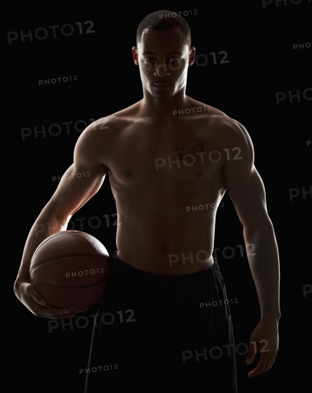 Studio portrait of shirtless man holding basketball. Photo : Mike Kemp