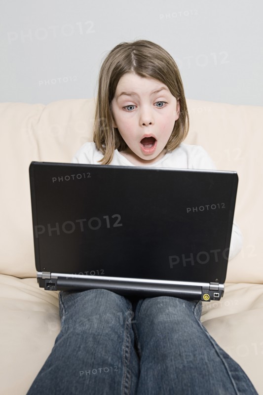 Girl (6-7) with laptop sitting on sofa. Photo: Justin Paget