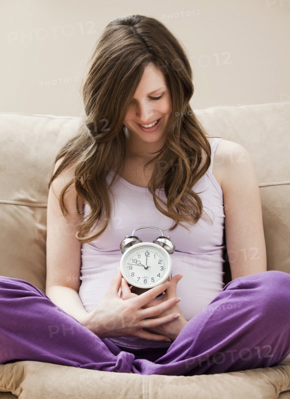 Young pregnant woman holding alarm clock. Photo: Mike Kemp