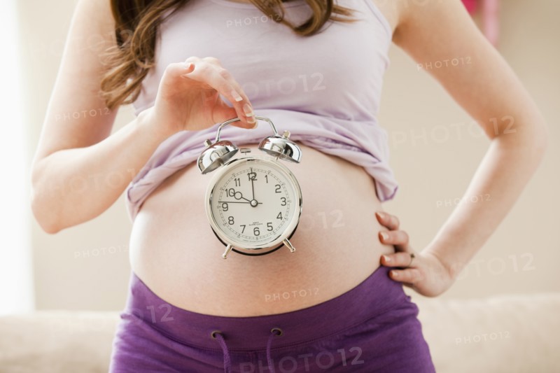 Young pregnant woman holding alarm clock. Photo: Mike Kemp