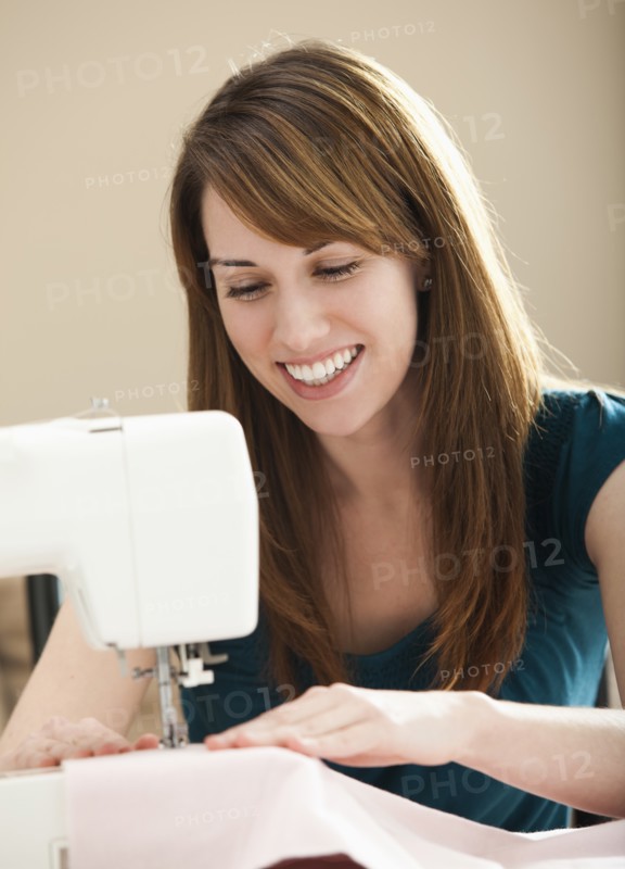 Smiling young woman using sewing machine. Photo : Mike Kemp