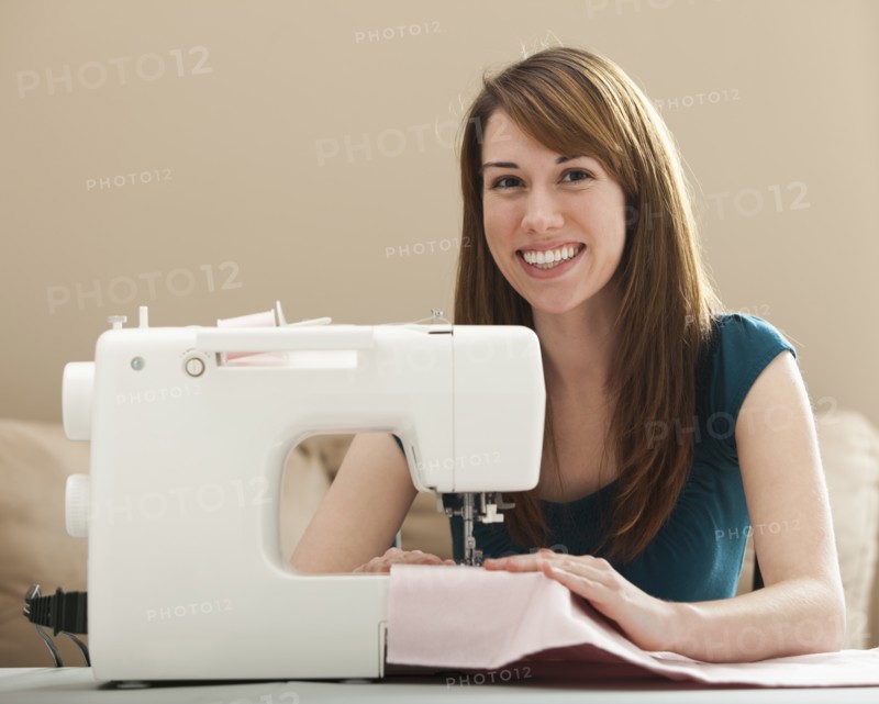 Portrait of smiling young woman using sewing machine. Photo : Mike Kemp